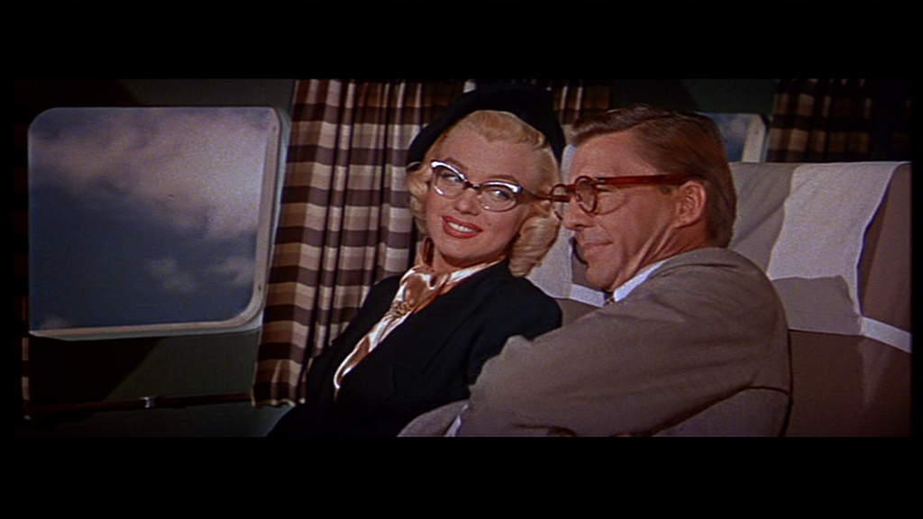 Marilyn Monroe as Pola, wearing glasses, getting comfortable talking to David Wayne, as Freddit, in the adjoining airplane seat in How to Marry a Millionaire.